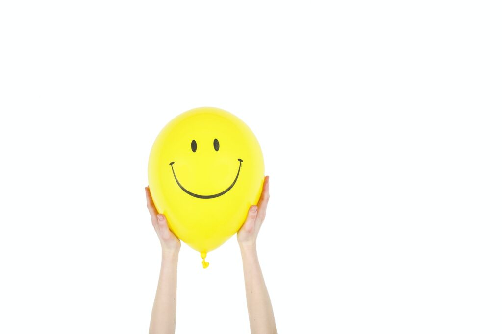 person holding yellow smiley balloon